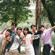 a group of young people standing next to each other in front of trees and water