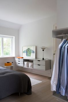 a bedroom with a bed, dresser and clothes hanging on the rails in front of a window