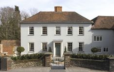 a large white house with a gate in front of it and bushes on the other side