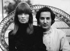 two people sitting in a wicker chair with their arms around each other and looking at the camera