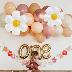 a baby is sitting in front of balloons with the word one on it and flowers