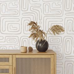 a vase with some plants in it sitting on a wooden cabinet next to a wallpaper