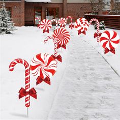 candy canes are lined up in the snow near a house on a snowy day