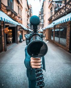 a person holding a camera in the middle of a street with buildings and shops on both sides