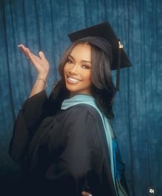 a woman wearing a graduation gown and holding her hand up in the air while smiling