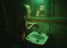 a woman standing in front of a mirror next to a sink under a faucet