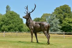 a statue of a deer standing on top of a lush green field with trees in the background