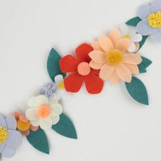 an arrangement of felt flowers on a white surface with green leaves and orange, pink, blue, and yellow flowers