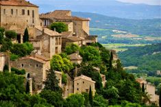 an old village on top of a hill with lots of trees in the foreground