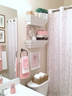 a white toilet sitting next to a bathroom sink under a mirror with pink towels hanging on it