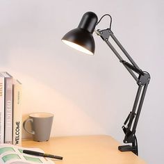 a desk lamp sitting on top of a wooden table next to books and a cup