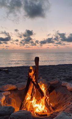 a campfire on the beach with rocks and water in the background