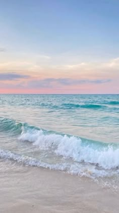 an ocean beach with waves coming in to shore and the sun setting on the horizon