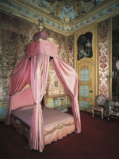 a pink canopy bed sitting in a bedroom next to a mirror