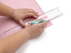 a baby's hand holding a measuring tape over a pink mat with a ruler on it