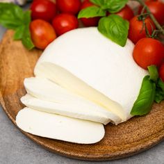 mozzarella cheese, tomatoes and basil on a wooden platter with green leaves