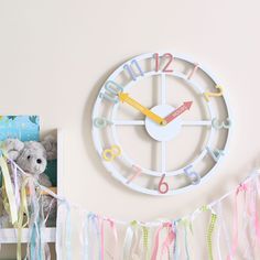 a clock on the wall with streamers hanging from it's sides and a teddy bear next to it