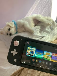 a small dog laying on top of a bed next to a nintendo wii game controller