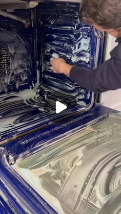 a man is painting the inside of an oven with blue and silver paint on it