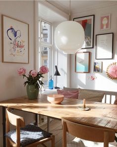 a dining room table and chairs with pictures on the wall behind it, in front of a window