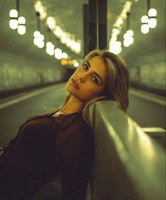 a woman sitting on a bench in an empty subway station looking up at the camera