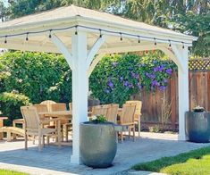 a white gazebo sitting on top of a lush green field next to a wooden table and chairs