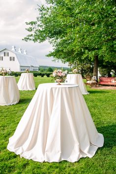 the table is covered with white cloths for an outdoor wedding reception in front of a barn