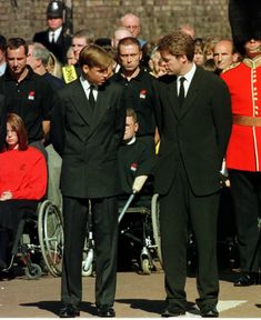 two men in suits and ties standing next to each other with people watching them from behind