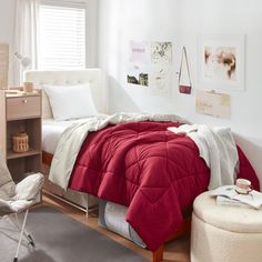 a bedroom with white walls and red comforter on the bed in front of a window