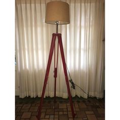 a red tripod floor lamp sitting in front of a window