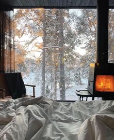 a bed in a room with a view of the snow covered trees and forest outside