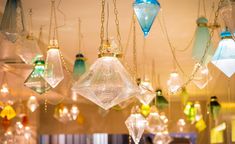 many different colored glass ornaments hanging from the ceiling in a room with lights and chandeliers