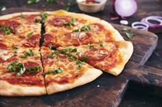 a pizza sitting on top of a wooden cutting board next to onions and pepperoni