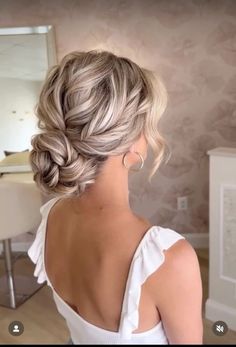 a woman with blonde hair in a white top is looking into the mirror and has her back to the camera