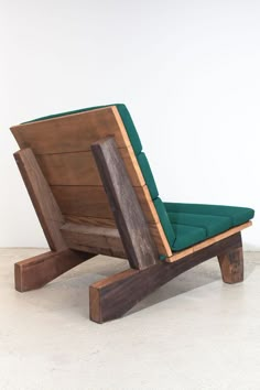 a chair made out of wood and green fabric on top of a white floor next to a wall