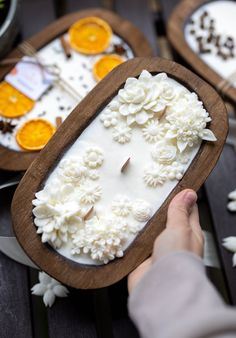 a person is holding a wooden tray with white frosting flowers on it and oranges in the background