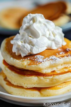 a stack of pancakes topped with whipped cream on top of each other and sitting on a white plate