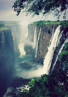 a rainbow shines in the sky over a large waterfall with water cascading it's sides