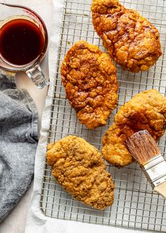 three fried chicken on a cooling rack next to a cup of tea and a brush