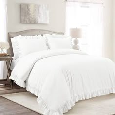 a white bed with ruffled sheets and pillows