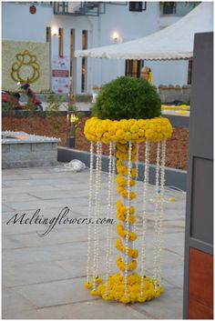 a yellow flower arrangement on the ground in front of a white building with flowers hanging from it's sides