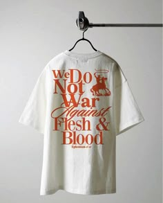 a white t - shirt with words on it hanging from a clothes hook in front of a wall