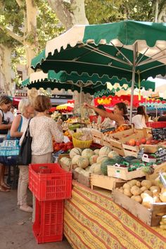 people are shopping at an outdoor market with fruits and veggies under umbrellas