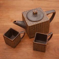 three pieces of tea set sitting on top of a wooden table next to each other