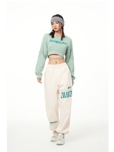 a young woman is standing in front of a white background wearing sweatpants and a green crop top