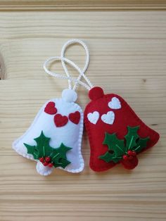 two felt christmas bells hanging from strings on a wooden surface with hearts and holly leaves