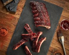 ribs on a cutting board with sauces and seasoning next to the meat that has been cut into pieces