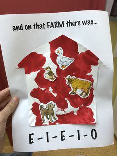 a child's hand holding up a piece of paper with farm animals on it