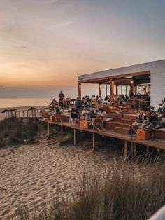 people are sitting at tables on the beach by the water and watching the sun go down