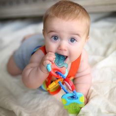 a baby laying on top of a bed chewing on a toy